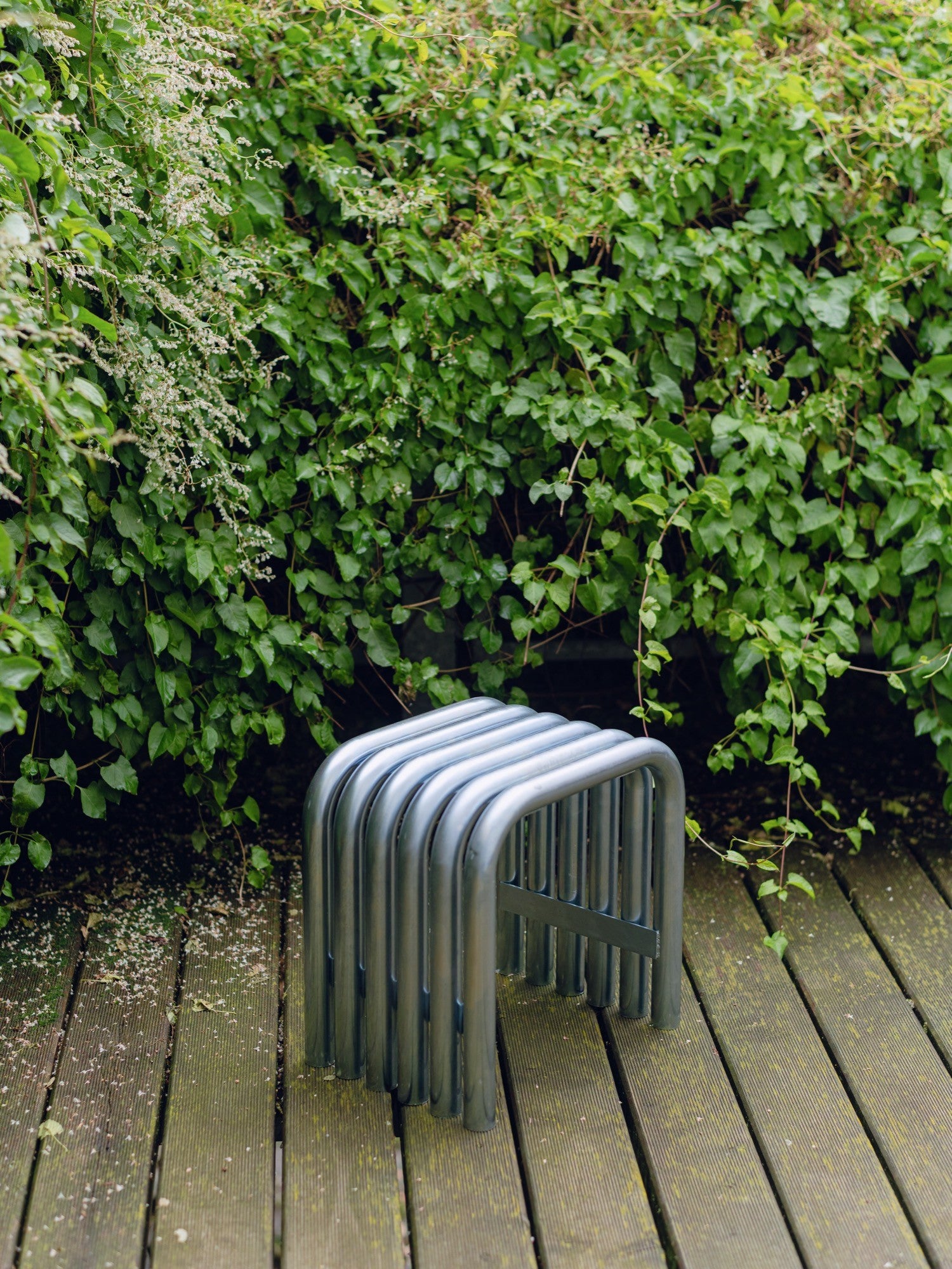noo.ma Nokk Stool, an industrial chic metal stool crafted from multiple bent matte grey powder-coated steel tubes, creating a distinctive ribbed, minimalist design. This contemporary outdoor stool or accent table offers durable, modern seating. Ideal for garden patios, balconies, or as brutalist-inspired indoor furniture.
