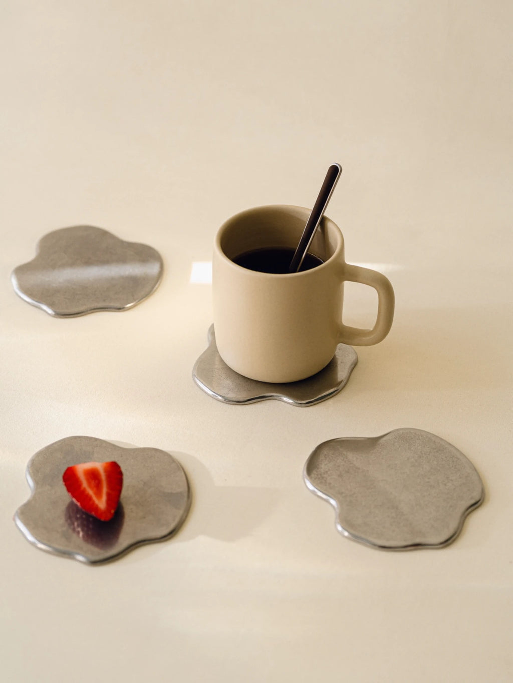 noo.ma Plama Stainless Steel Coaster - Set of 4, a set of four modern minimalist coasters with a distinctive organic, fluid blob shape, crafted from durable brushed silver stainless steel. These contemporary metal coasters provide stylish table protection for drinks and elevate the aesthetic of living room coffee tables or dining room surfaces.