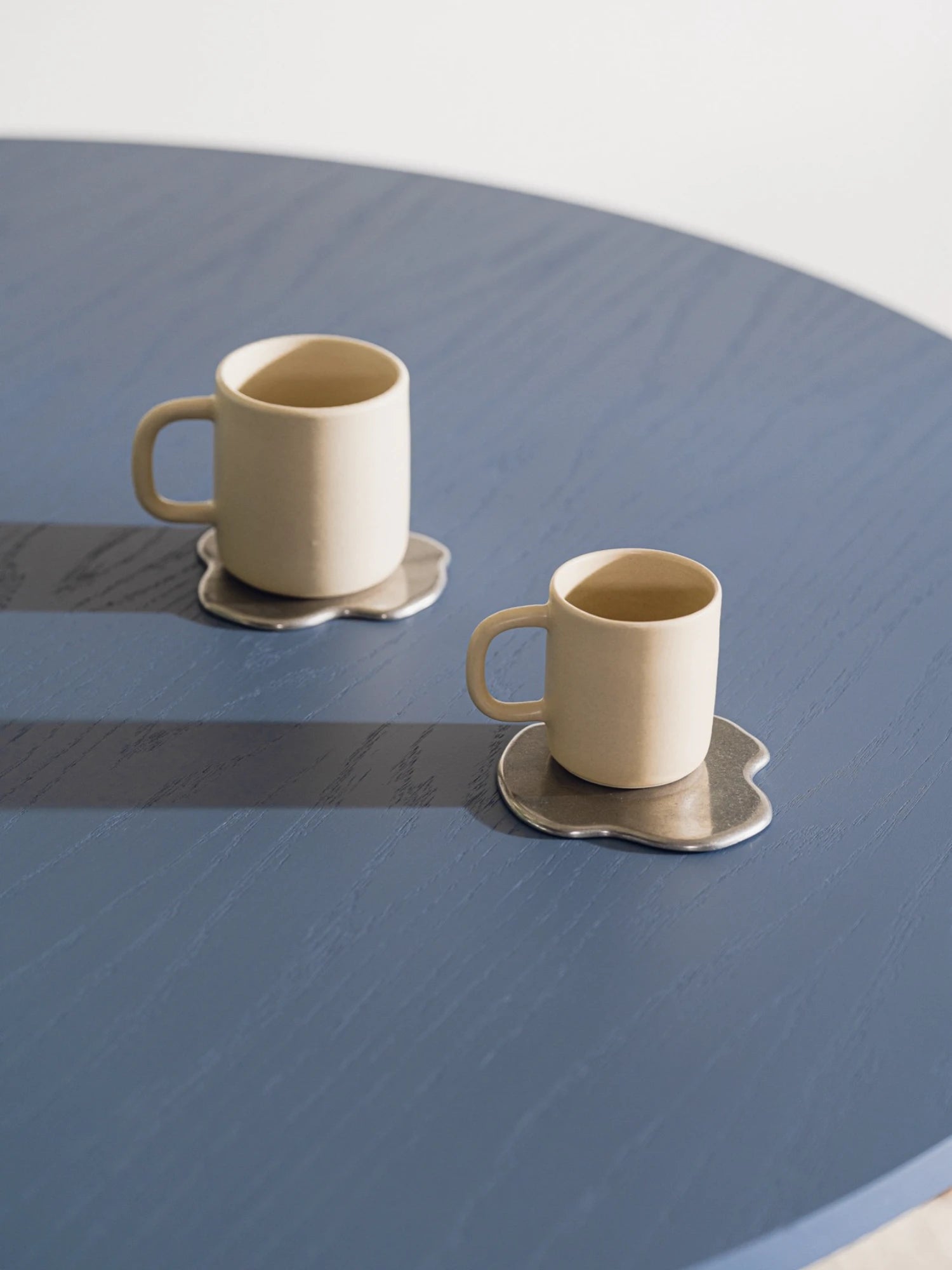 Two ceramic mugs with saucers on a blue surface