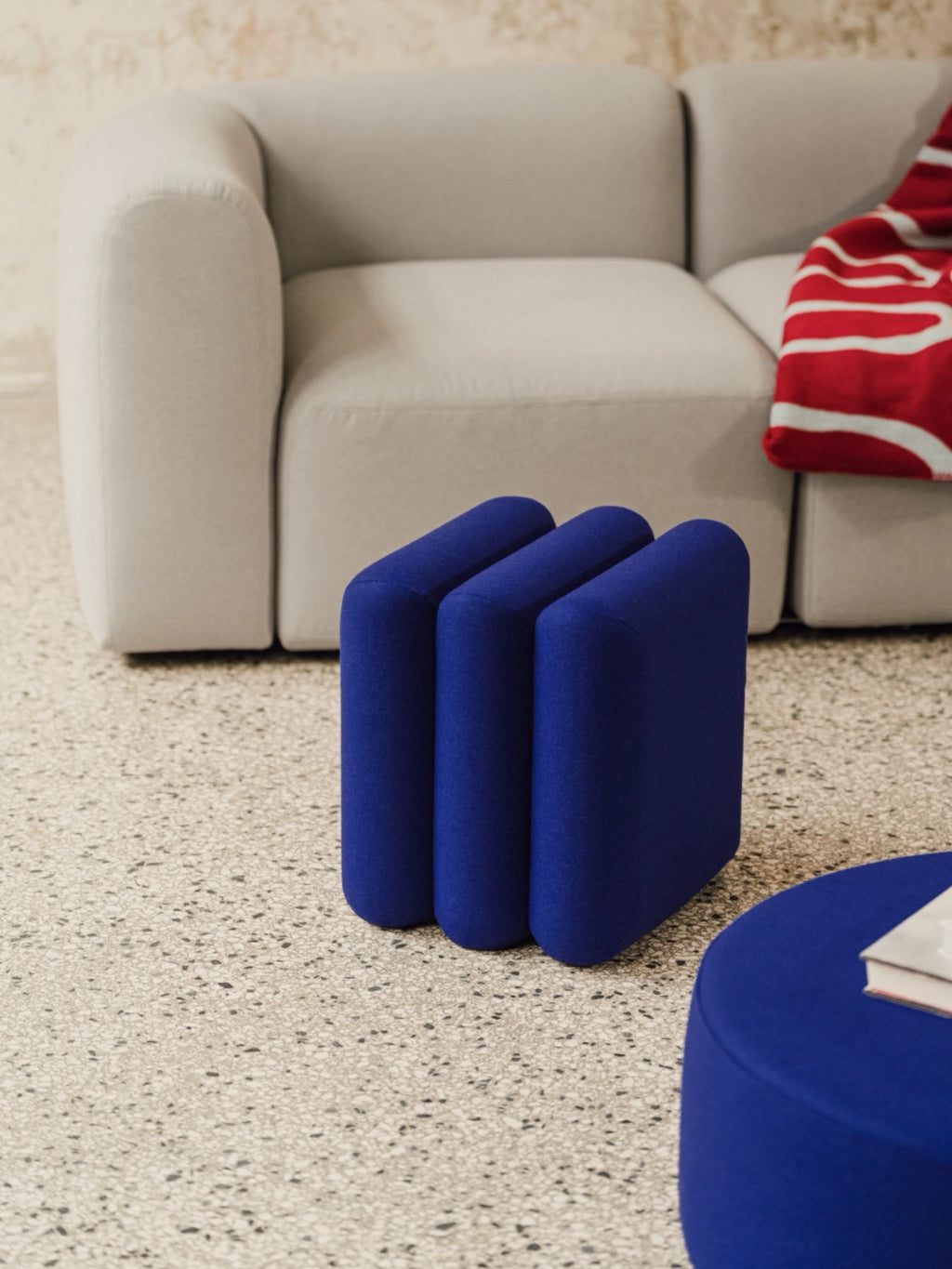 noo.ma Radd Pouf, a vibrant royal blue fabric pouf featuring a unique sculptural design with three connected, rounded upholstered segments. This contemporary ottoman offers a playful yet modern aesthetic with its soft texture and bold color. Perfect as an accent stool or extra seating in a modern living room, bedroom, or creative lounge space.