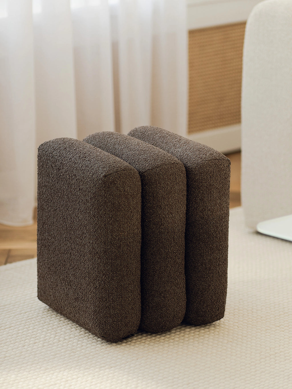 noo.ma Radd Pouf, a dark chocolate brown upholstered pouf crafted with a rich, textured bouclé-like fabric, featuring a distinctive sculptural design of three integrated, rounded vertical.