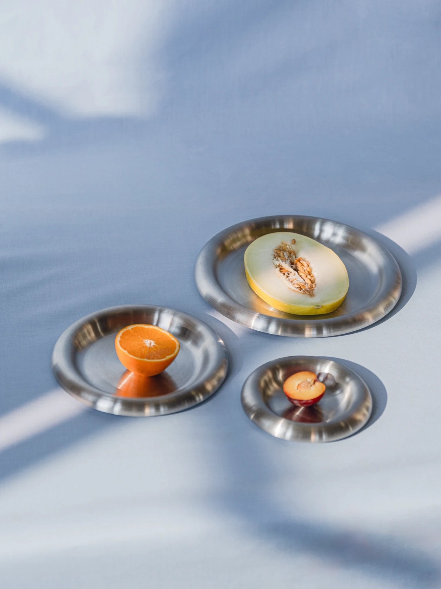 Three small metal plates with fruits on a light blue background