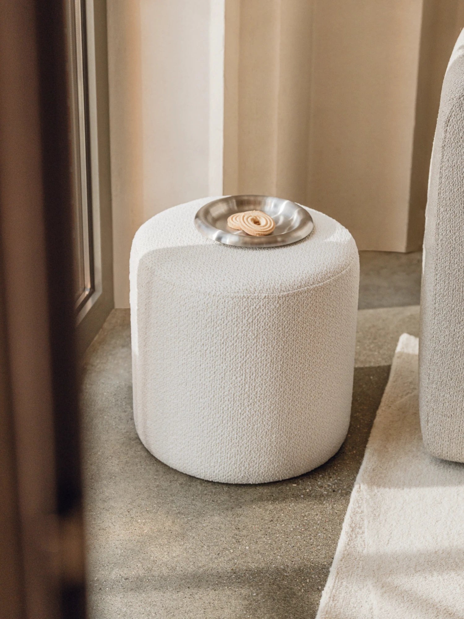 Round textured ottoman with a metallic plate on a neutral background