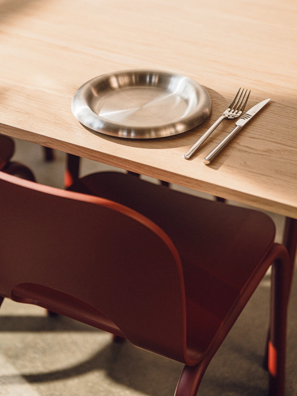 Silver plate and cutlery on a wooden table with a red chair.
