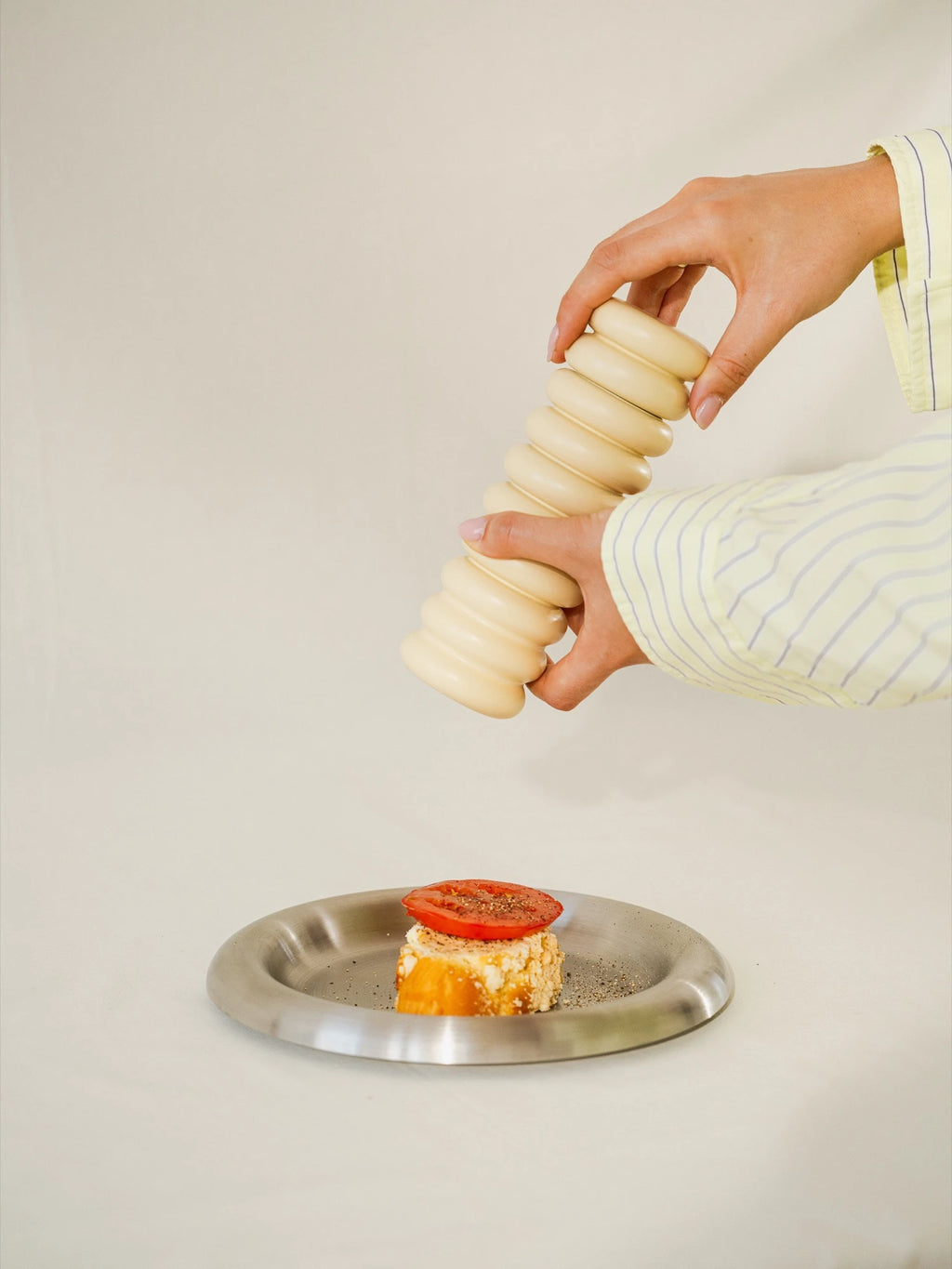 Person using a pasta spiralizer on a plate with pasta and tomato.