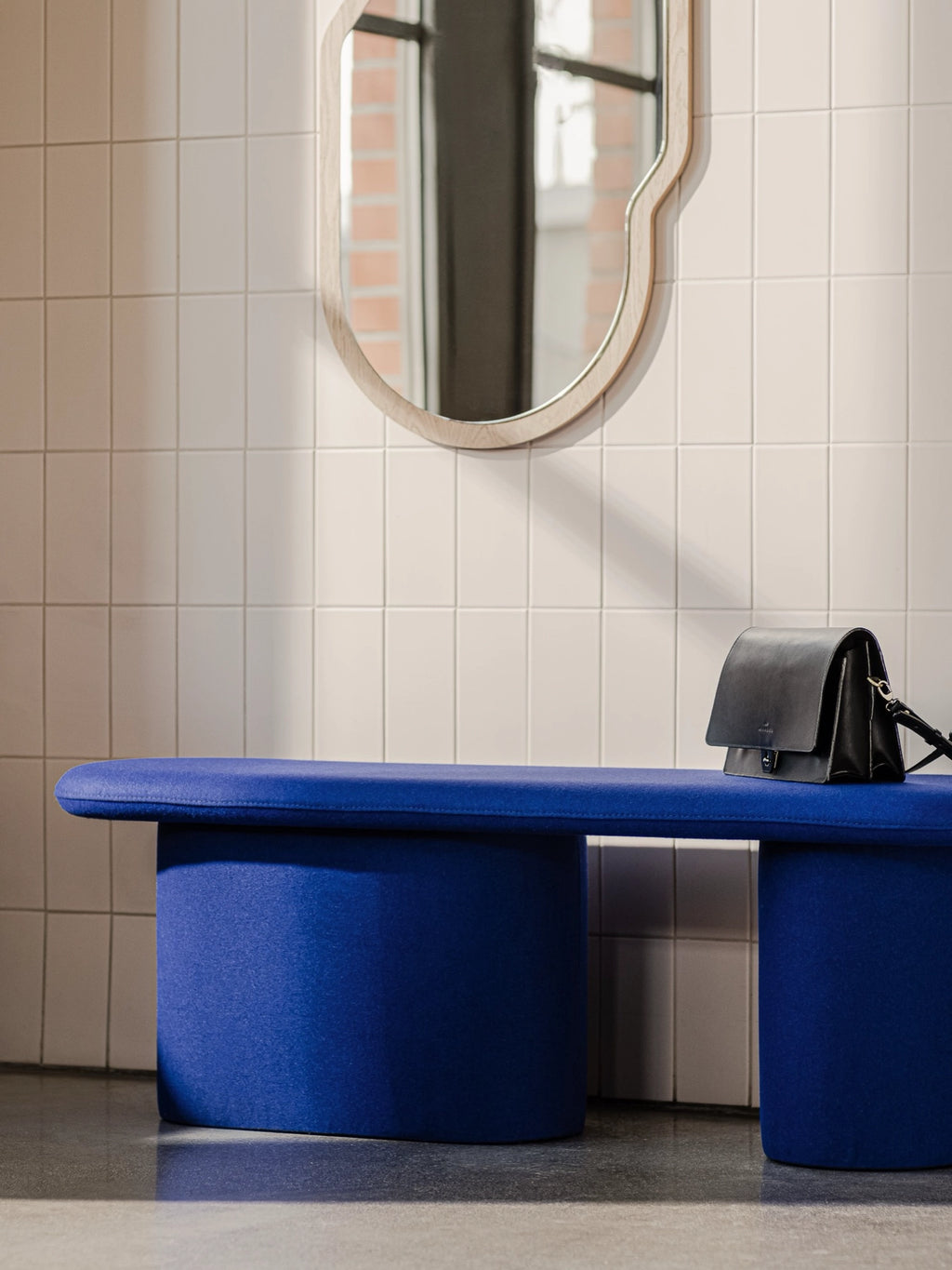 noo.ma Rull Bench, a striking royal blue upholstered bench with a modern minimalist organic design, featuring a plush, rounded seat and two robust cylindrical legs. This contemporary fabric bench offers comfortable soft seating, ideal for a stylish entryway, Scandinavian living room, or as a vibrant bedroom accent.