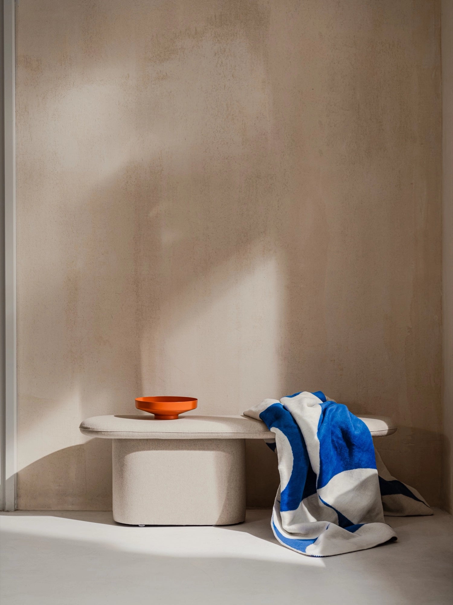 noo.ma Rull Bench, a modern minimalist upholstered bench featuring a soft, organic pill-shaped seat and a sturdy, rounded block base. Covered in a light beige, textured fabric, this contemporary bench offers a clean Scandinavian aesthetic. Ideal for adding versatile seating to an entryway, bedroom, or living room in an organic modern home.