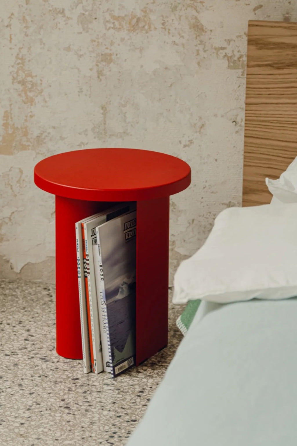 noo.ma Sato Side Table, a vibrant red modern minimalist side table crafted from smooth powder-coated metal with a sleek cylindrical base and round tabletop. This contemporary end table features an integrated vertical slot, making it a functional magazine holder for organized storage. Perfect as a bold bedside table, living room accent, or industrial chic nightstand for design-conscious interiors.