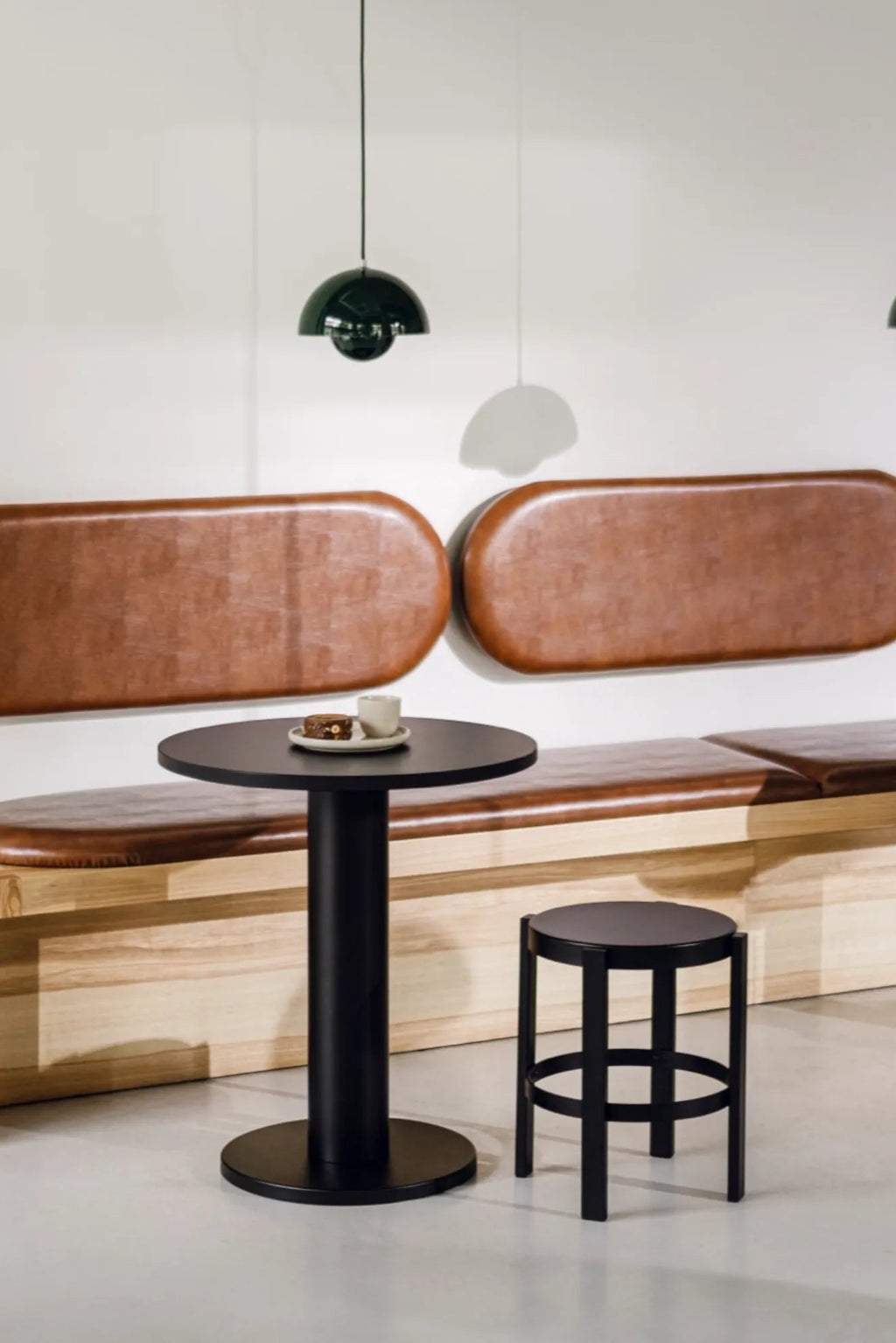 noo.ma Sool Café Table, a sleek matte black metal dining table featuring a round tabletop and a sturdy cylindrical pedestal base, embodying modern minimalist design. This contemporary bistro table is perfect for compact dining areas, Scandinavian kitchens, or stylish café interiors.