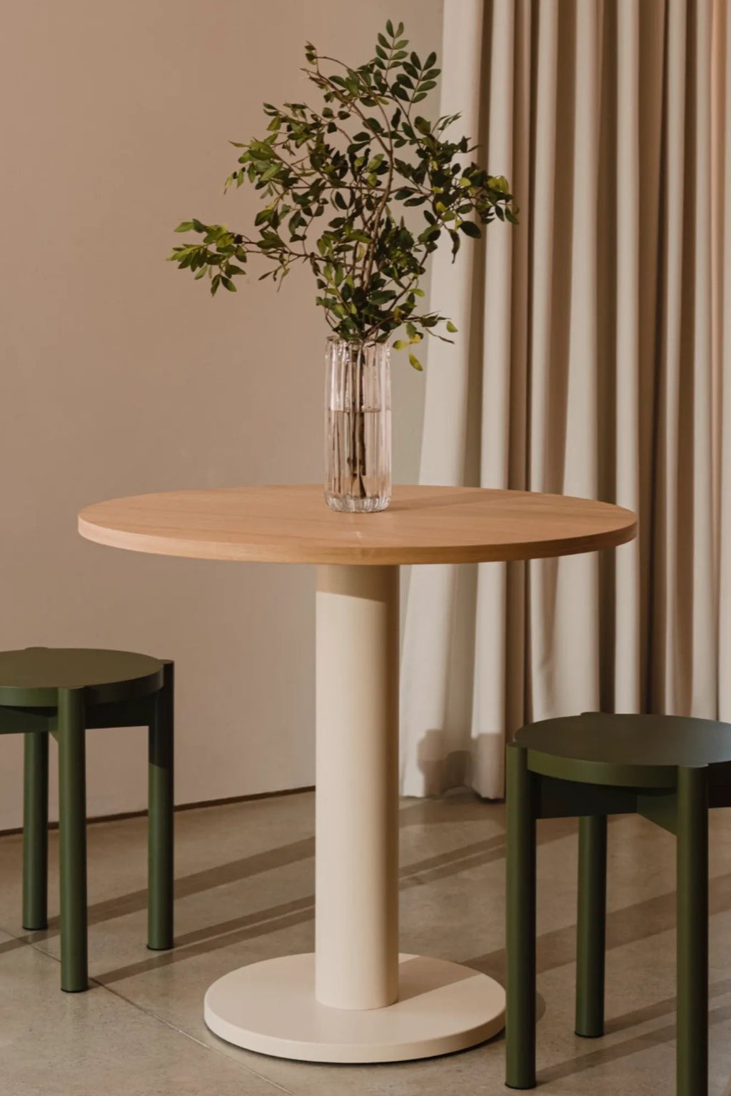 noo.ma Sool Café Table, a modern minimalist round dining table featuring a light natural wood tabletop and a sturdy, matte cream-colored cylindrical pedestal base with a matching round foot. This Scandinavian-inspired bistro table is perfect for small apartment dining rooms, kitchen breakfast nooks, or contemporary café settings.