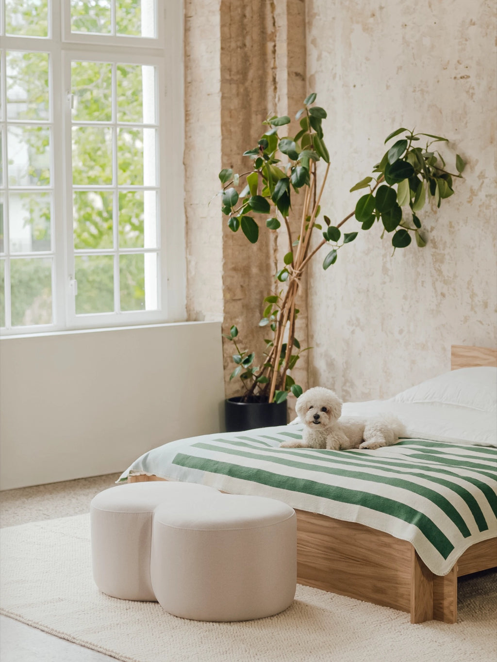 noo.ma Umbo Pouf, an organic modern pouf featuring a distinctive curved, clover-like shape with two conjoined rounded sections, upholstered in a soft light beige fabric. This sculptural accent seating piece brings minimalist style to any contemporary bedroom, living room, or cozy reading nook.