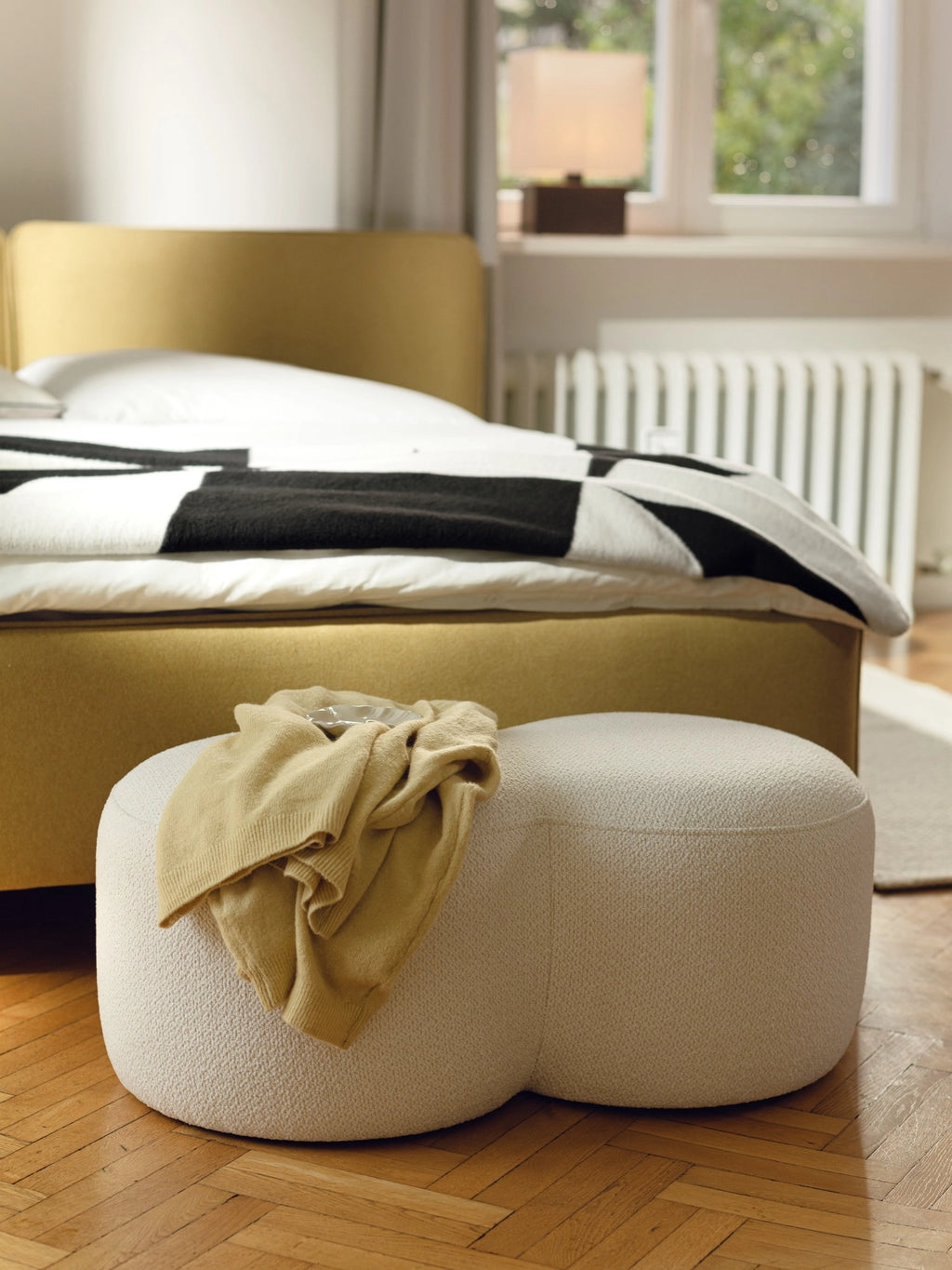 noo.ma Umbo Pouf, a sculptural, organically shaped pouf featuring two rounded, connected lobes, upholstered in a luxurious cream bouclé fabric with a rich, textured finish. This low-profile, contemporary ottoman adds organic modern elegance to living rooms, bedrooms, or cozy reading nooks.