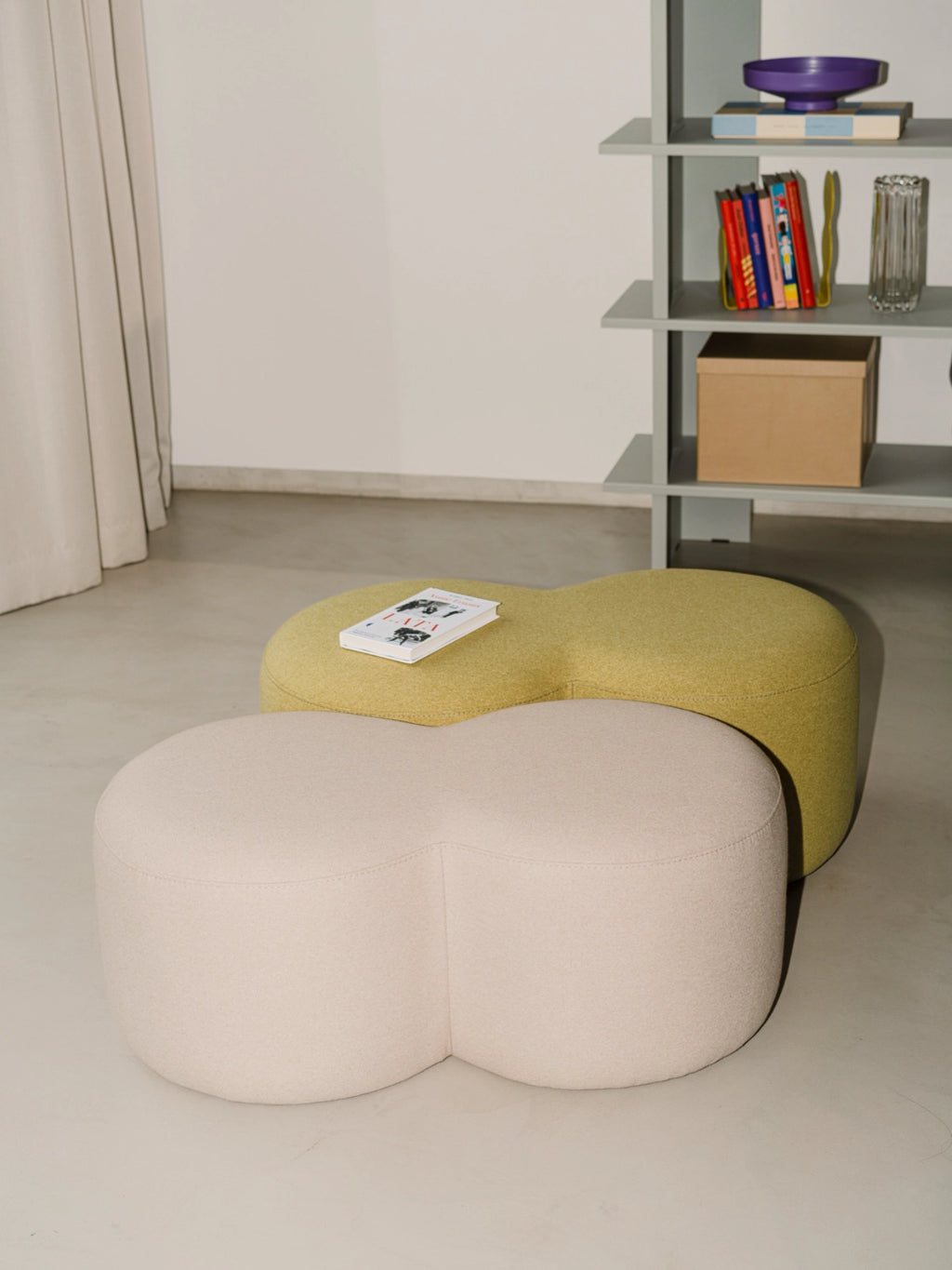 noo.ma Umbo Pouf, an organic modern pouf set featuring a distinctive double-lobed, peanut-shaped silhouette, upholstered in soft, textured bouclé fabric. The set includes a light beige/off-white pouf and a vibrant olive green/chartreuse pouf, perfect for adding cozy accent seating to a Scandinavian living room, contemporary bedroom, or creative lounge area.