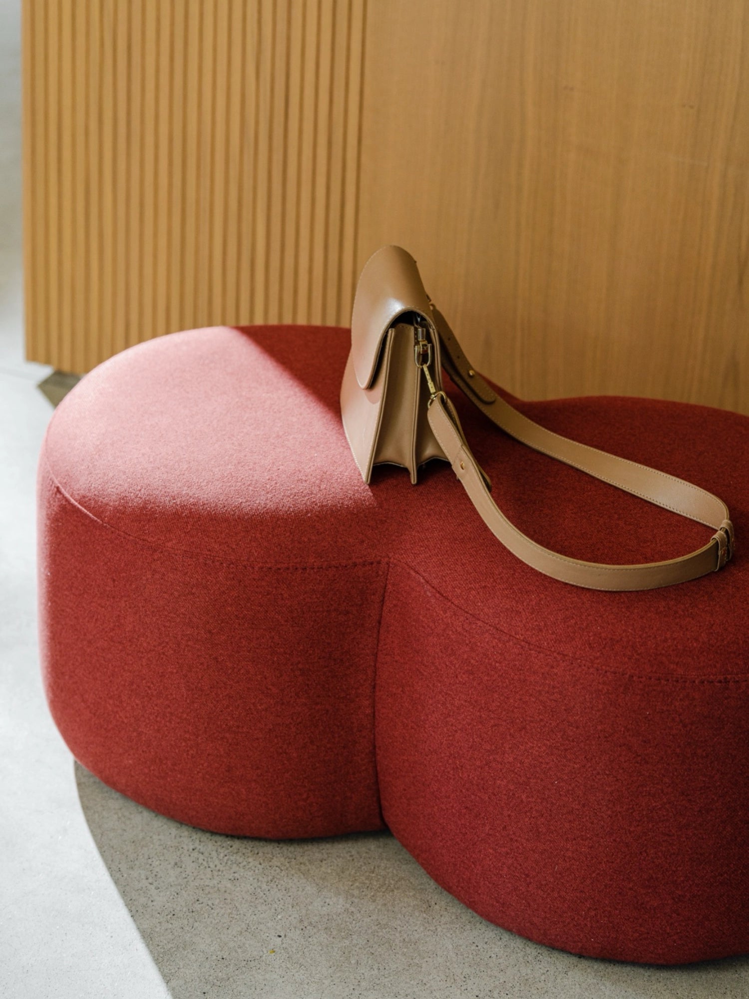 noo.ma Umbo Pouf, an organic modern upholstered pouf in a deep terracotta red, featuring a soft, textured fabric and a unique biomorphic, rounded shape composed of two connected lobes. This contemporary minimalist ottoman is perfect for adding a cozy design accent to Scandinavian living rooms, bedrooms, or reading nooks.