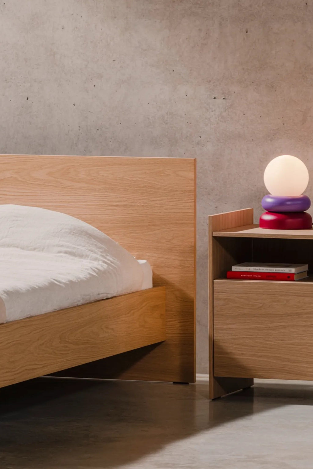 noo.ma Valt Bed, a modern minimalist bed frame crafted from solid oak wood with a light natural finish and prominent grain. It features a clean-lined rectangular headboard and a sturdy, low-profile platform design, embodying Scandinavian design principles. Perfect for contemporary bedrooms seeking an organic modern aesthetic or a light wood bed solution.