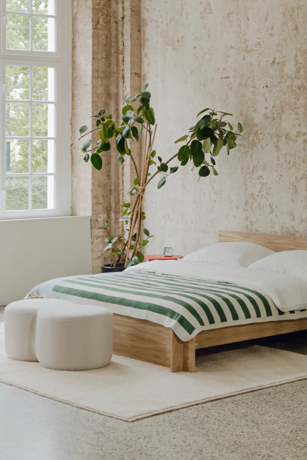 noo.ma Valt Bed, a modern minimalist platform bed crafted from light natural wood with a simple, clean-lined design and a low-profile headboard. This Scandinavian-inspired solid wood bed frame features crisp white bedding topped with a forest green and white striped blanket. Ideal for creating a serene and contemporary bedroom aesthetic.