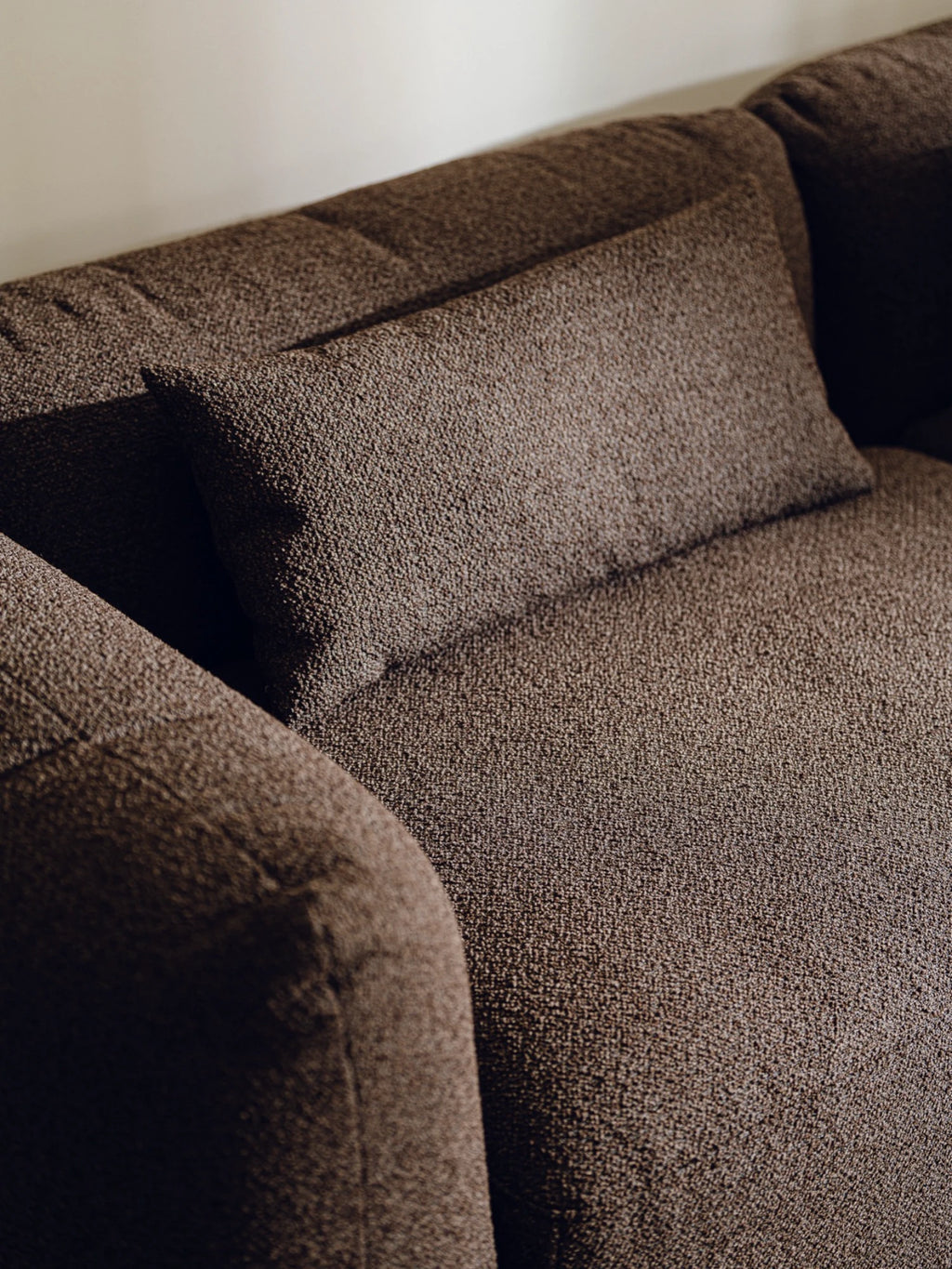 noo.ma Yaro Sofa, a modern dark brown sofa upholstered in a rich, textured woven fabric with a distinctive nubby or bouclé-like surface, featuring plush deep seating and a soft, inviting armrest. This contemporary design with subtle tufted back cushions is perfect for creating a cozy yet stylish focal point in a minimalist living room or organic modern interior.