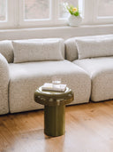 Green side table with a glass of water and book in front of a beige sofa.