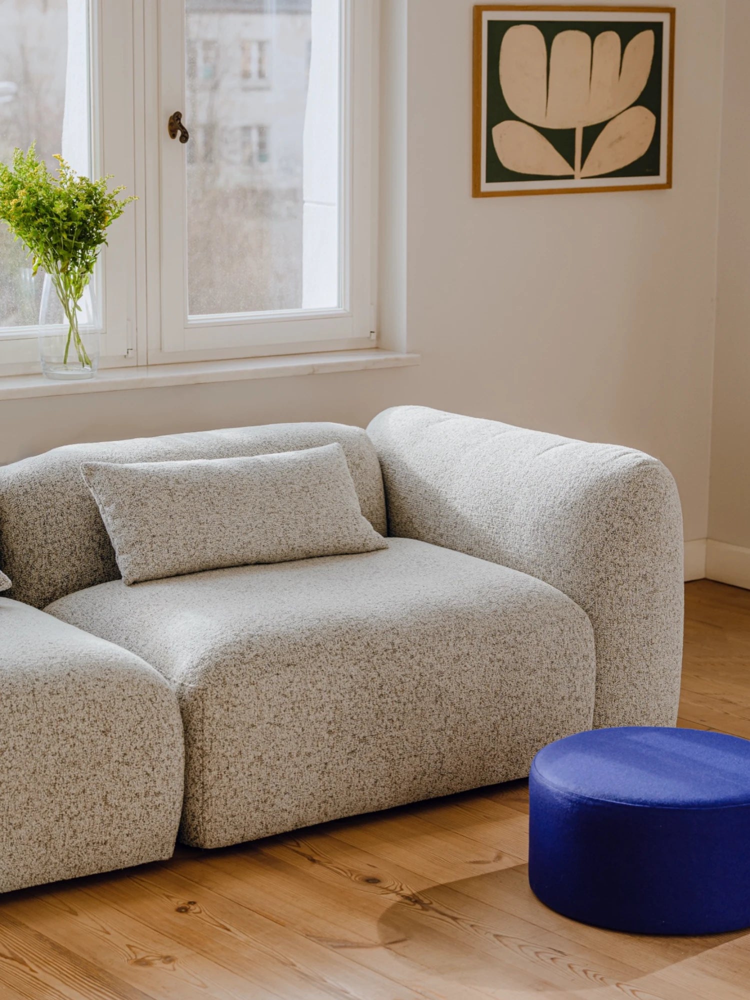 Beige sofa with a blue ottoman in a room with a window and wall art.