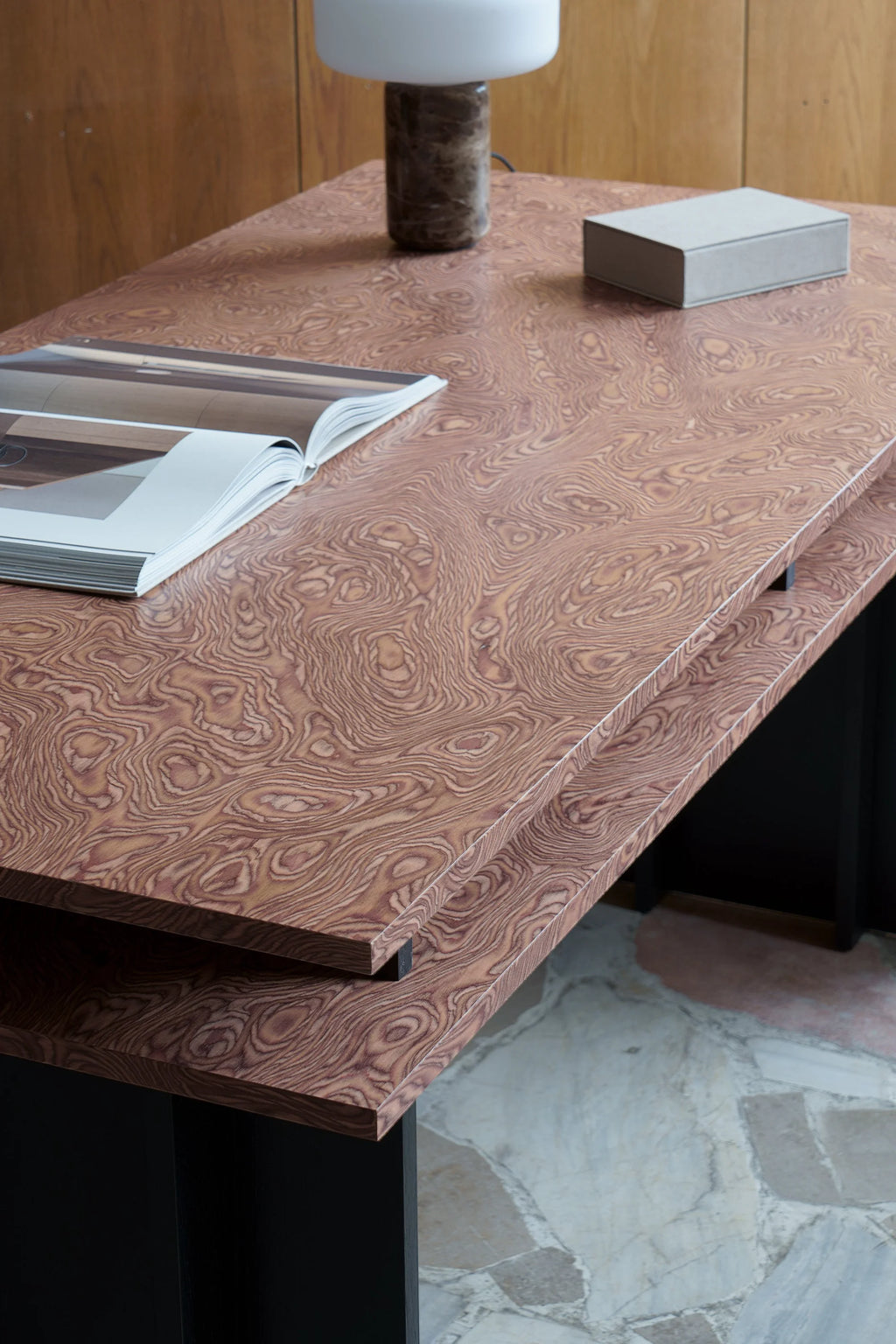 TAMO Piato Desk featuring rich brown and beige swirled wood grain, a modern design with stacked tiers, and a sturdy black base. A premium workspace solution for any home office or study.