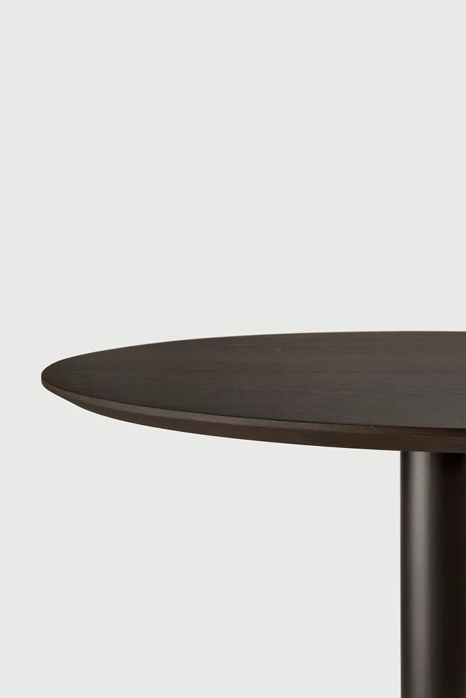 Ethnicraft Blend Round Dining Table, a modern minimalist dining table crafted from dark solid oak with a rich espresso finish and a smooth, round tabletop. It features a sturdy cylindrical base, creating a contemporary dark wood dining table ideal for elegant dining rooms or stylish open-plan kitchen spaces.