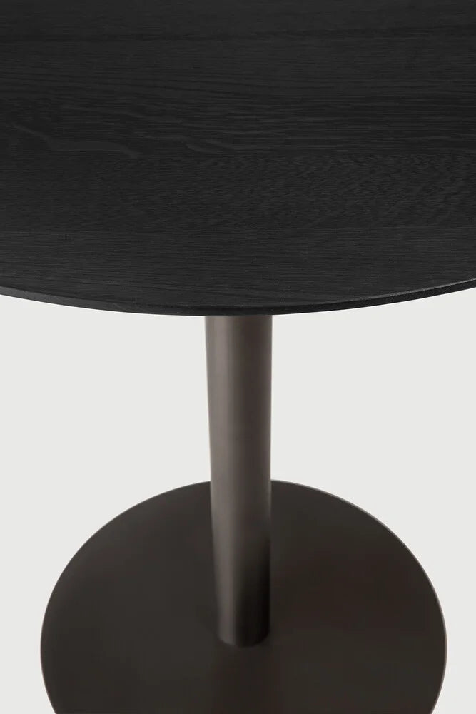 Ethnicraft Blend Round Dining Table, a modern minimalist dining table featuring a dark black oak round tabletop with visible wood grain texture, paired with a sturdy matte dark grey metal pedestal base. This contemporary solid wood dining table is perfect for elegant dining rooms or stylish kitchen areas.