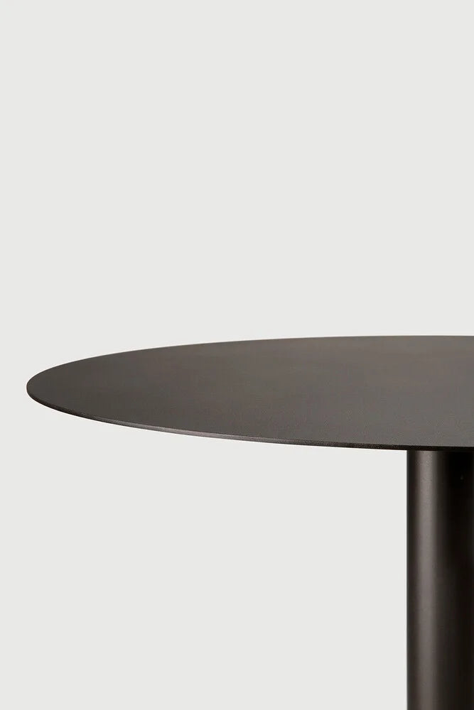 Ethnicraft Blend Round Dining Table, a modern minimalist round dining table crafted from matte black metal with a sleek, smooth tabletop and a sturdy cylindrical pedestal base. This contemporary black dining table offers a clean, refined aesthetic. Perfect for industrial chic dining rooms, small kitchens, or modern minimalist living spaces.