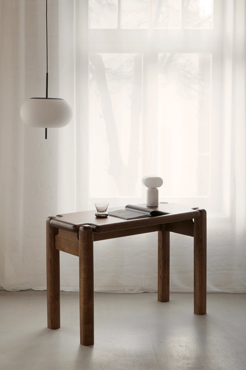 TAMO Puffo Desk, a premium mid-century modern solid wood desk with a rich brown finish and rounded edges, styled with a glass and magazine. Ideal for a contemporary office or living space.