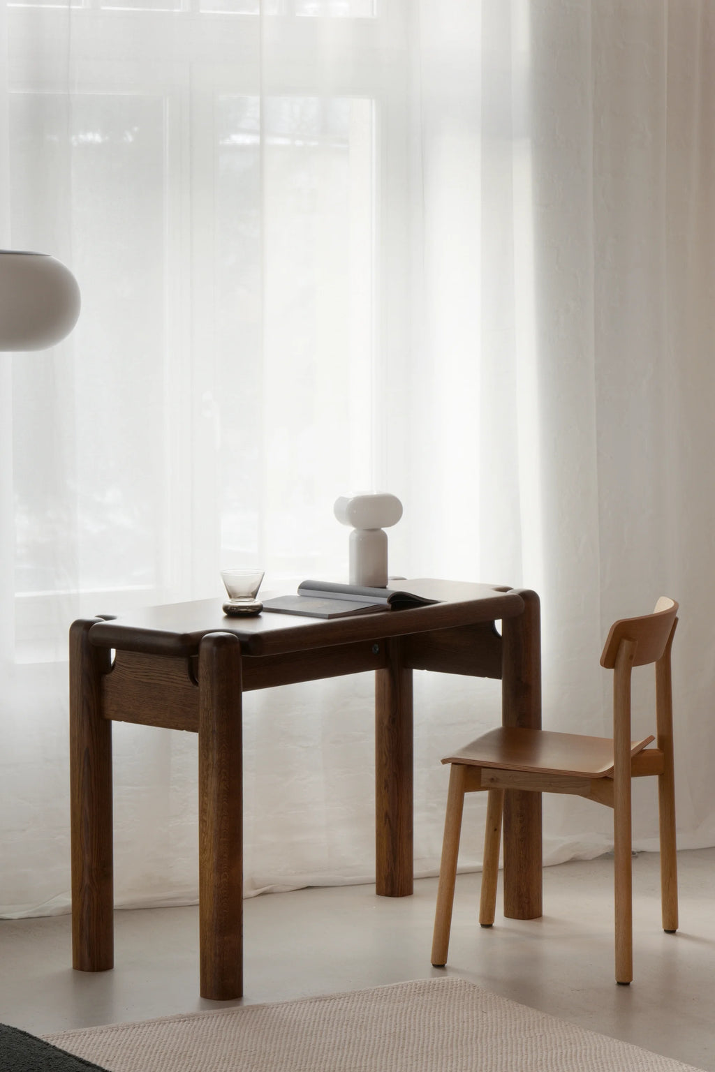 TAMO Puffo Desk, a luxury dark brown oak wood desk with thick rounded legs and subtle detailing, styled with a modern lamp. Perfect for a sophisticated home office.