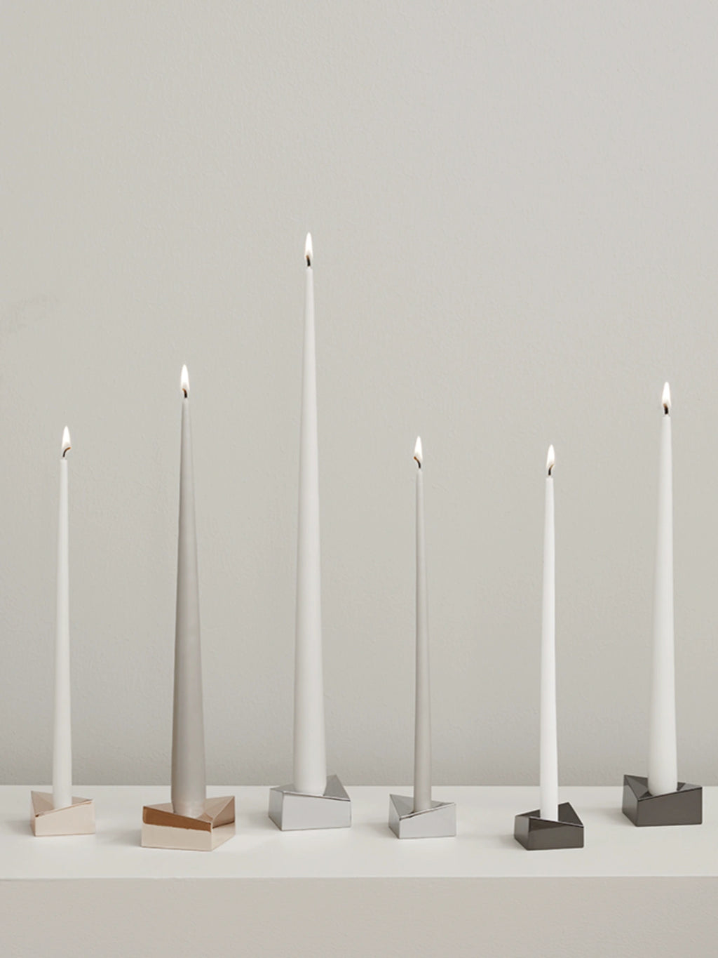 Stoff Nagel Reflect Candle Holder, a collection of modern minimalist metal candle holders with striking geometric, faceted bases in polished rose gold, shimmering silver, and deep gunmetal finishes.