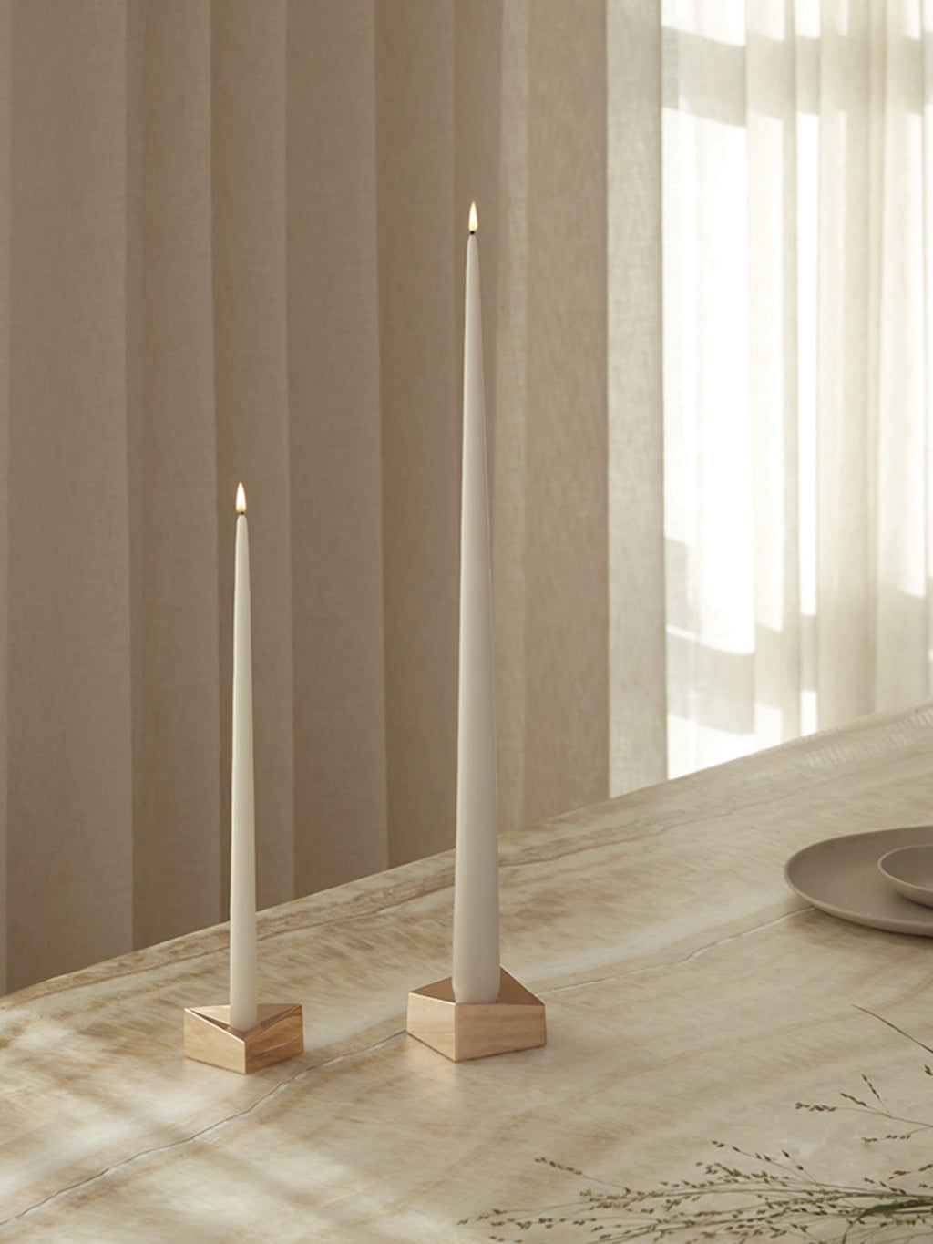Stoff Nagel Reflect Candle Holder, a modern minimalist solid wood candle holder featuring a light natural blonde wood finish and a unique geometric triangular cutout to securely hold a taper candle. This elegant wooden candle holder, shown as a set with varying heights, perfectly complements Scandinavian or Japandi dining table centerpieces and contemporary shelf styling.