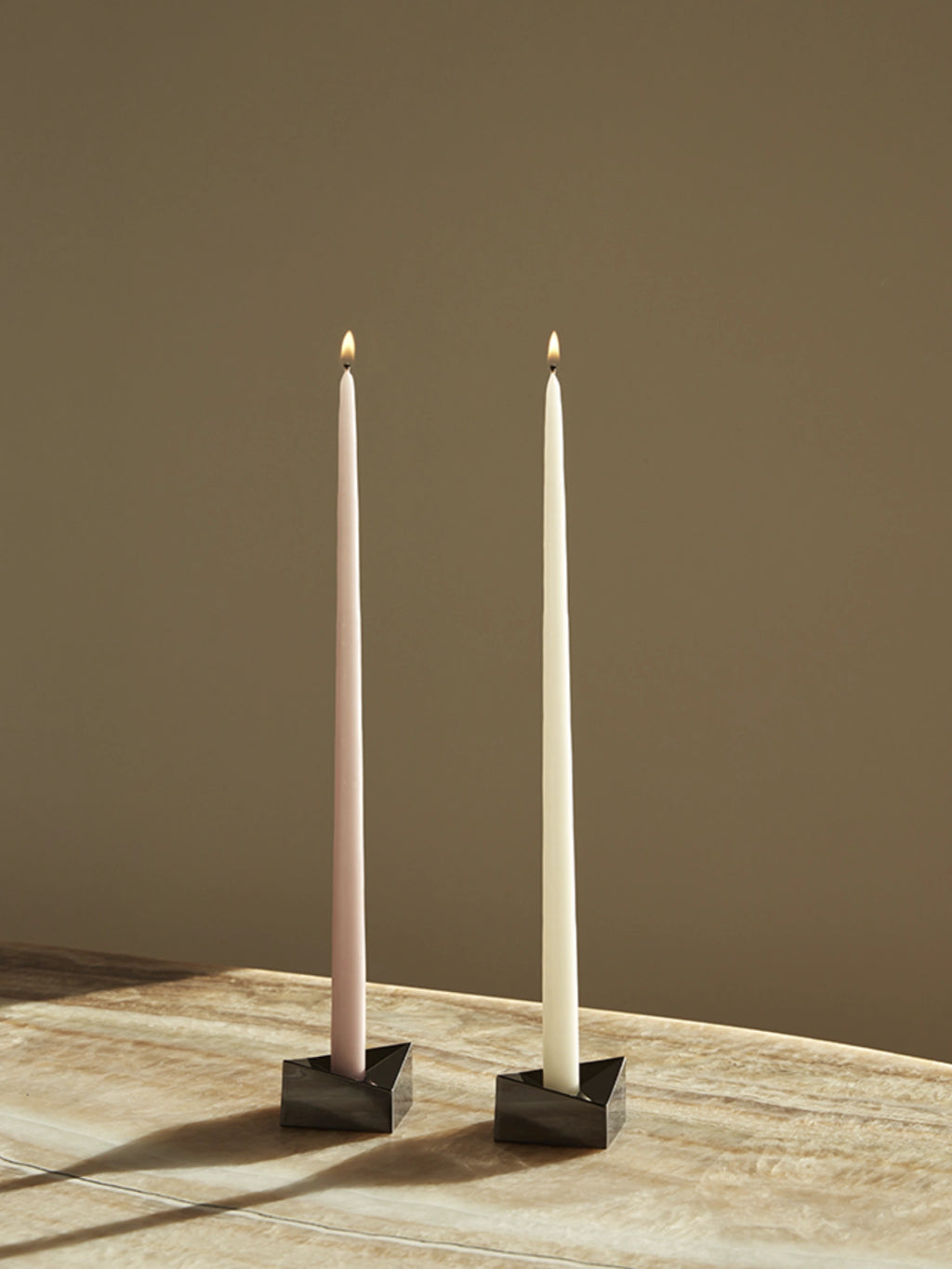 Stoff Nagel Reflect Candle Holder, a pair of modern minimalist candle holders crafted from dark matte metal with a striking geometric, triangular shape, designed to hold slender taper candles.