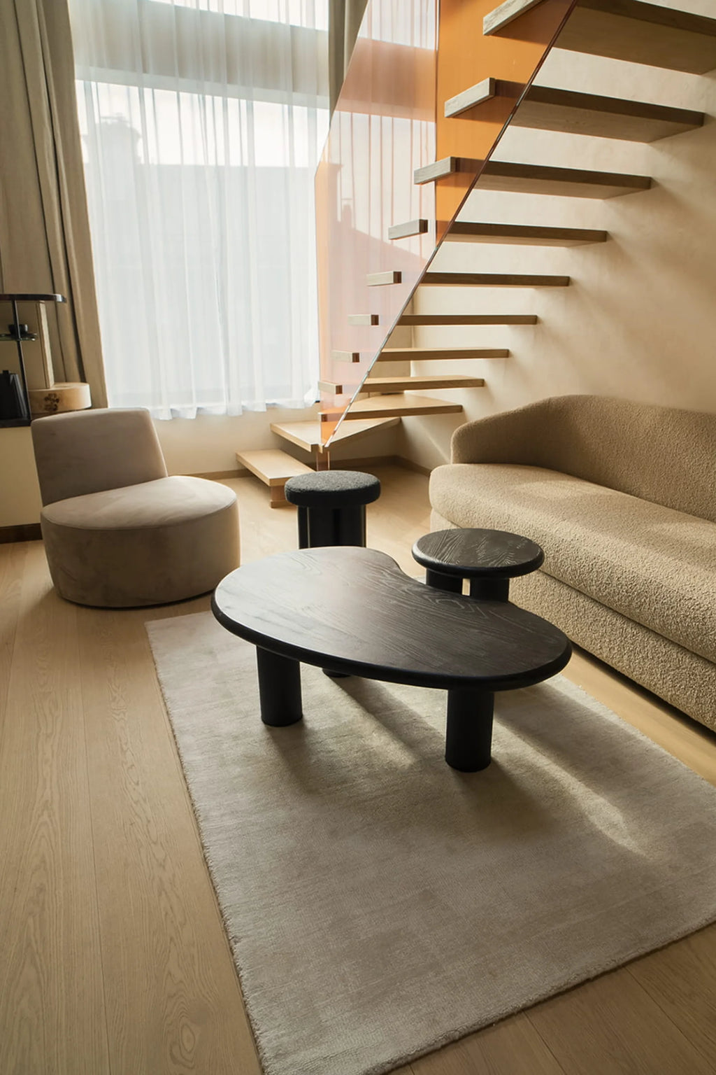NG DESIGN Object 061 Coffee Table in a lifestyle setting, featuring a dark stained wood top with an organic, kidney-bean shape and three cylindrical black legs. A smaller round side table attaches to it. This luxury, modern piece enhances contemporary living spaces.