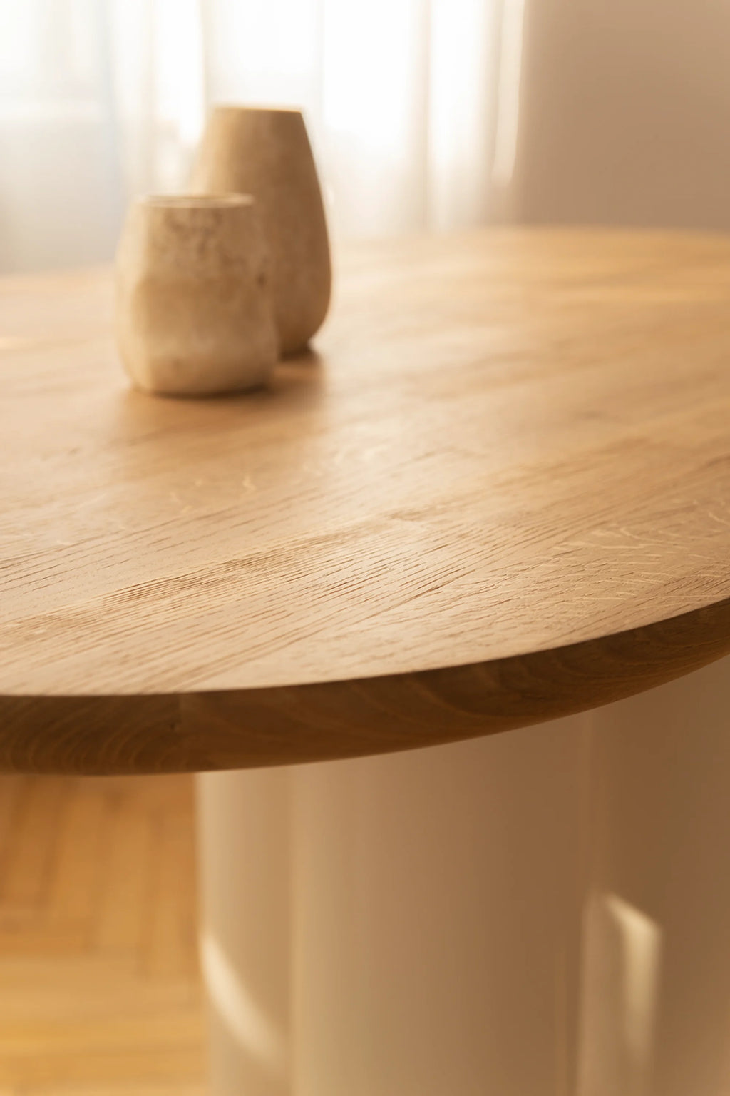 NG DESIGN Object 055 Dining Table, a close-up of the round, light oak wood grain tabletop with a thick, subtly tapered edge, resting on a white cylindrical base; two decorative brown ceramic vases sit on top. A premium, modern centerpiece for any dining space.
