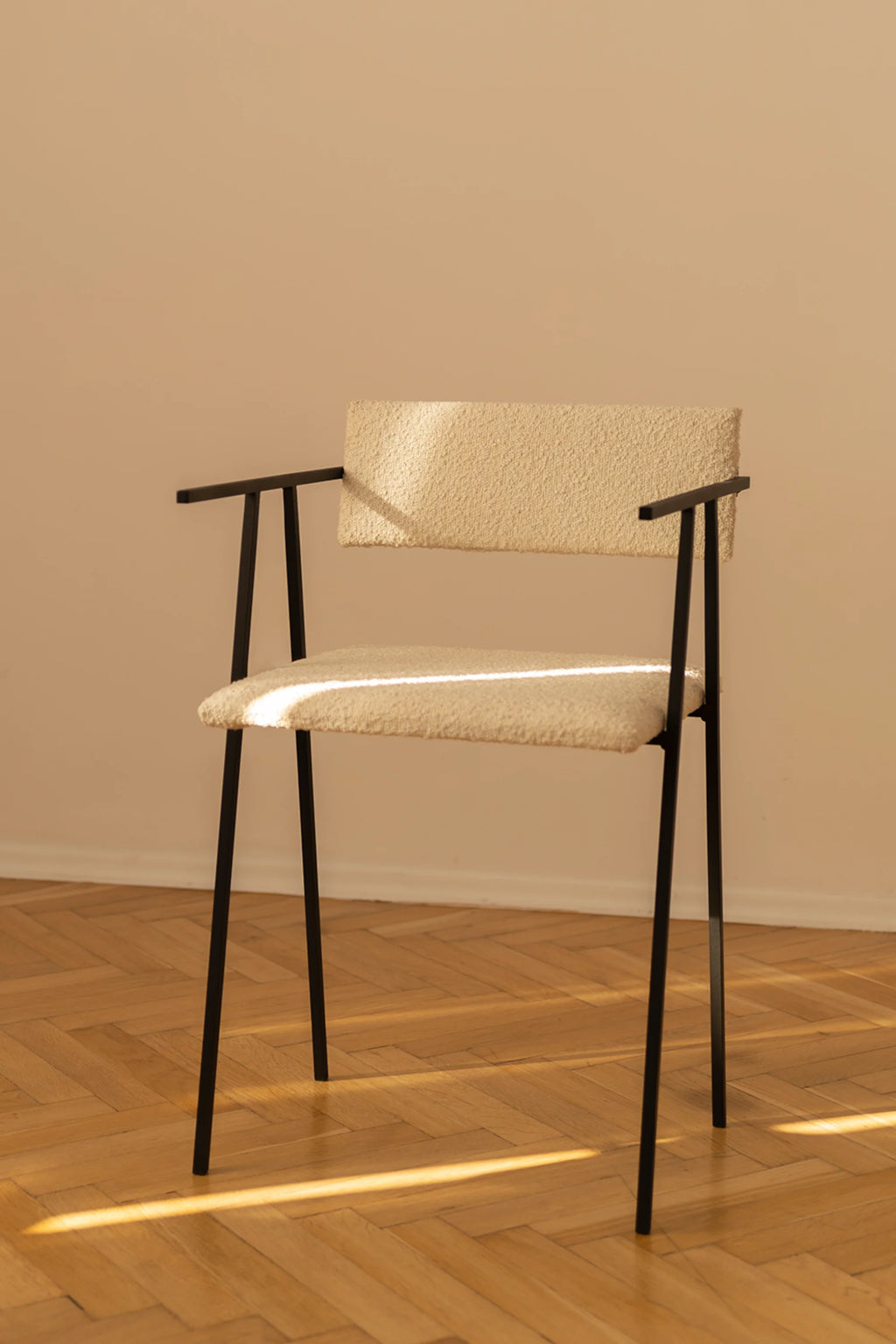 NG DESIGN Object 058 Chair, featured in a lifestyle shot with sunlight. This luxury modern chair has a cream bouclé upholstered back and seat, supported by sleek black metal legs and armrests. Perfect for contemporary interiors.