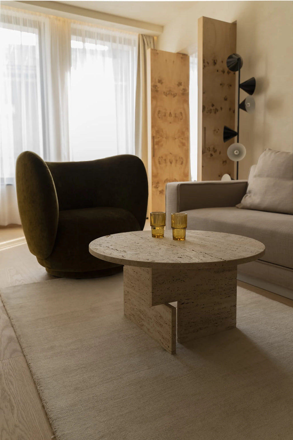 NG DESIGN Object 068 Coffee Table; a round, light beige porous travertine coffee table with a modern, sculptural base, styled in a luxurious living room. Perfect for contemporary interiors.