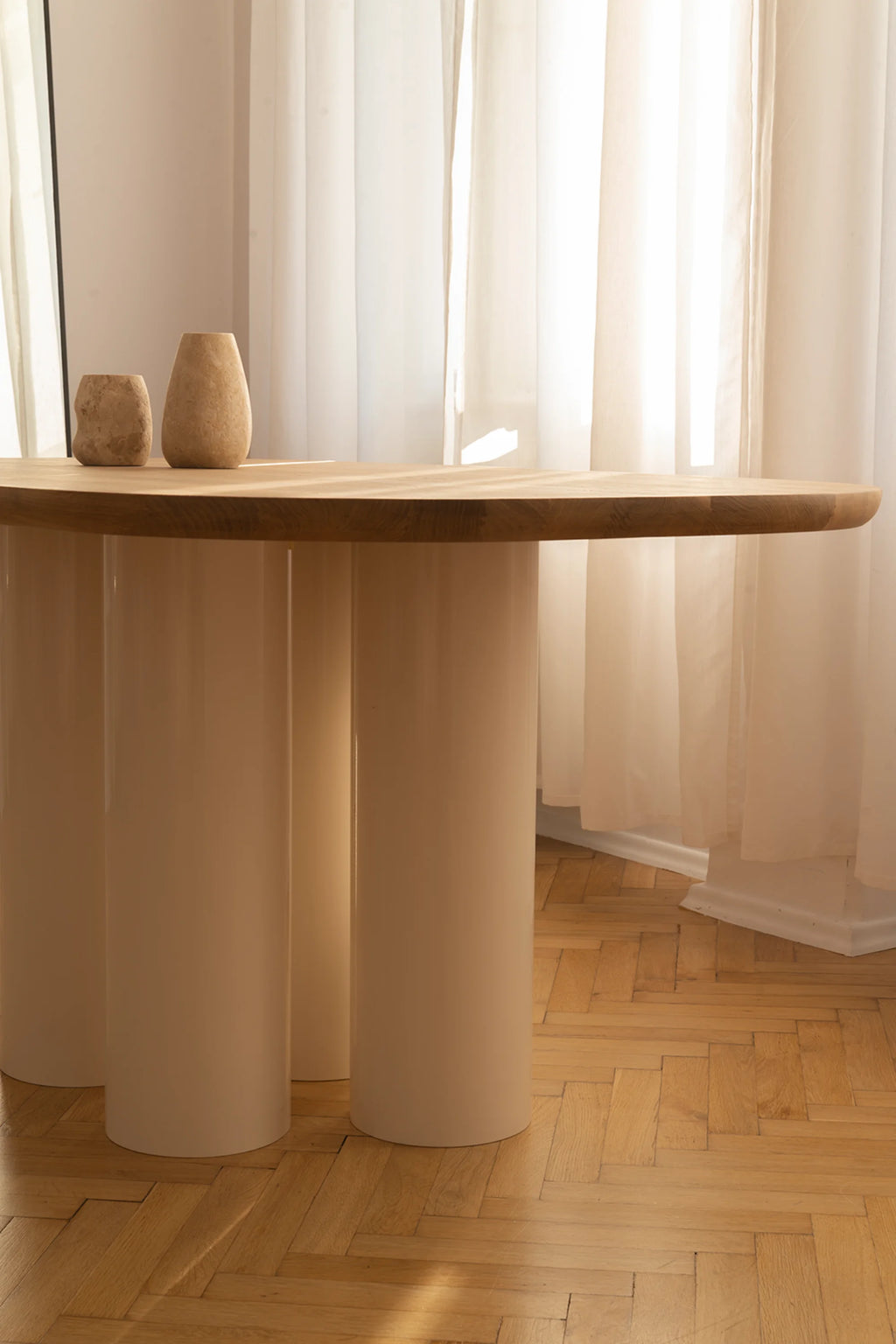 NG DESIGN Object 055 Dining Table, featuring a natural light-toned wooden top and four substantial cream-colored cylindrical legs. Two textured beige vases sit on its surface in a lifestyle setting with sheer curtains and hardwood herringbone floors. A premium, modern dining solution.