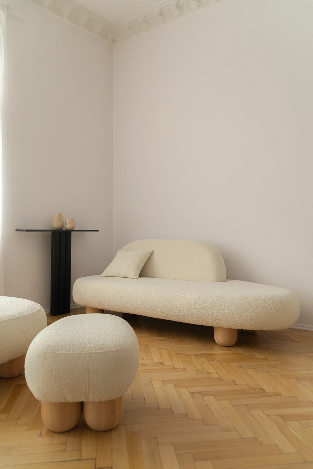 NG DESIGN Object 049 Pouf: Two creamy white bouclé poufs with light wooden legs, shown on a herringbone wood floor in a modern living space. This luxury accent piece is ideal for stylish interiors.