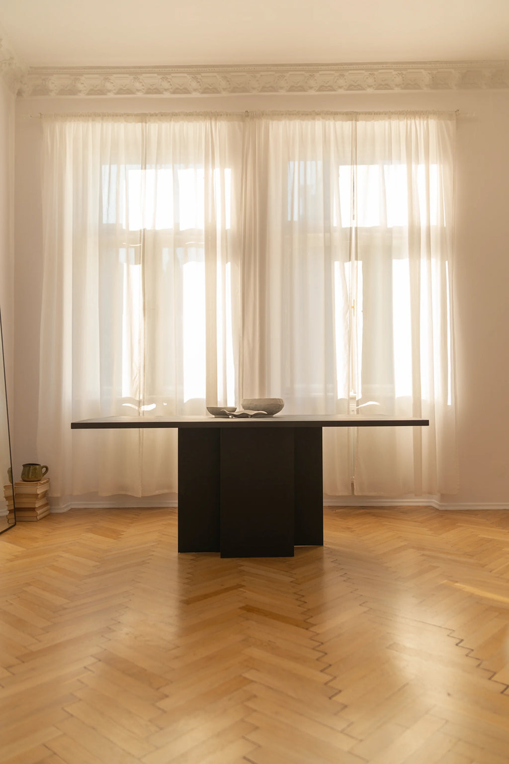NG DESIGN Object 056 Dining Table, featuring a sleek, rectangular black tabletop and innovative pedestal base. This luxury modern dining table is displayed in a sunlit room, accented with white sheer curtains and light wood herringbone flooring. Ideal for sophisticated interiors.