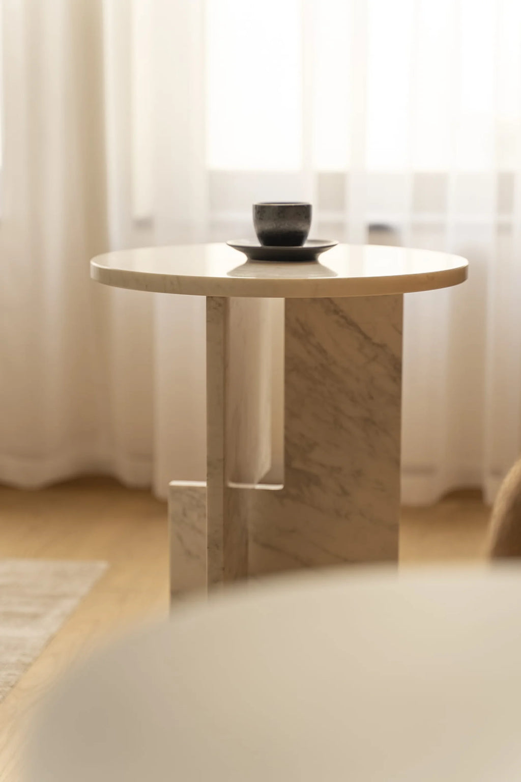 NG DESIGN Object 065 Side Table: A luxury round, polished light beige marble side table with a unique geometric marble base, styled with a dark ceramic cup and saucer. Perfect for modern living spaces.
