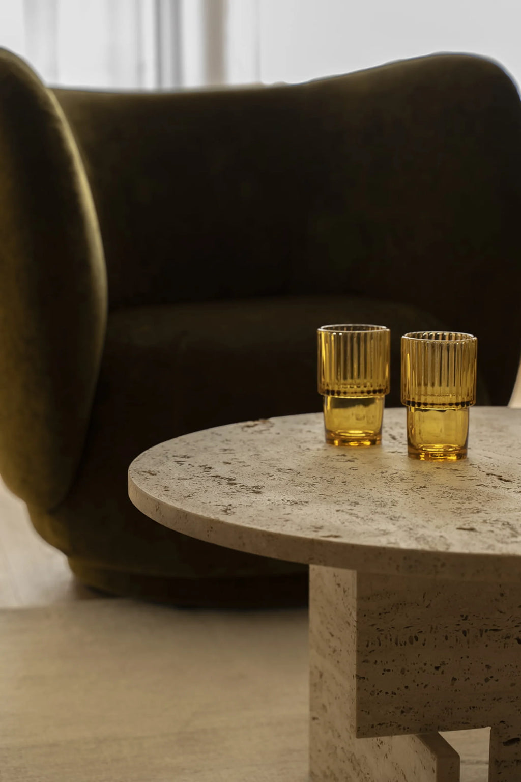 NG DESIGN Object 068 Coffee Table in a lifestyle shot, showcasing its light beige textured travertine surface and base, with two amber ribbed glasses. A premium furniture piece for any modern living space.