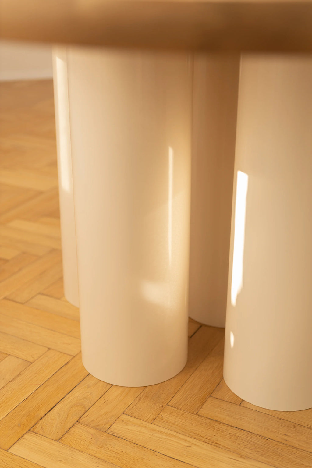 NG DESIGN Object 055 Dining Table, featuring round cream-colored matte lacquer legs on a light-colored herringbone wood floor, showcasing unique modern furniture design. A premium centerpiece for any dining space.