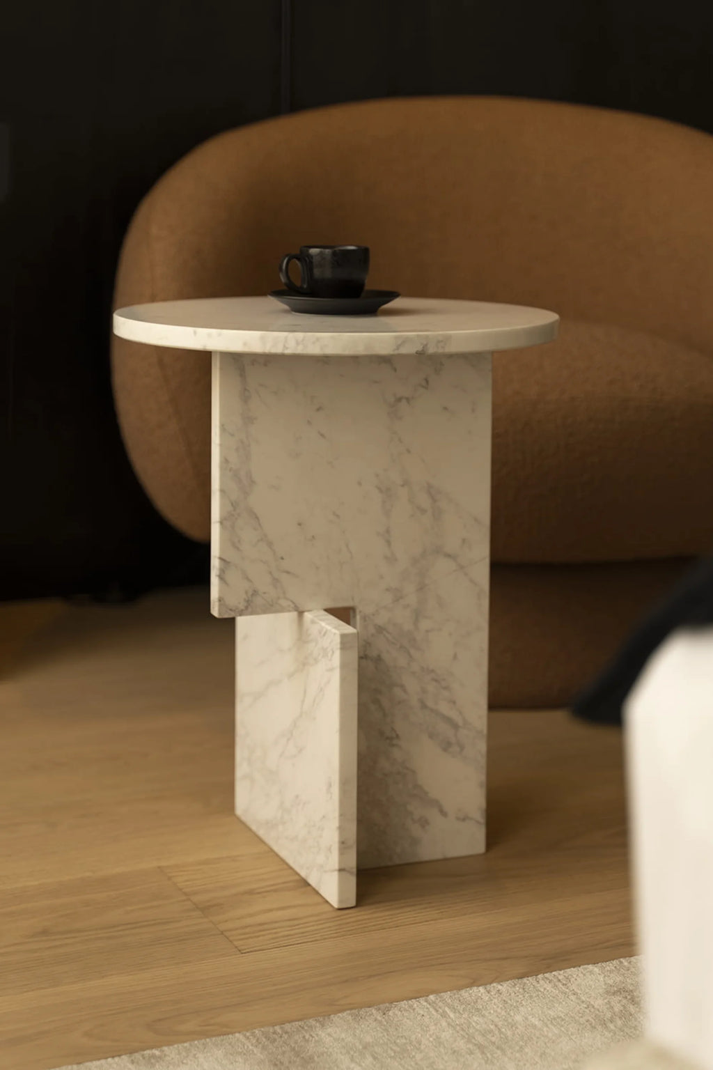 NG DESIGN Object 065 Side Table, a luxury white marble side table with gray veining and a unique offset rectangular base, displayed with a black coffee cup and saucer on light wood flooring in a lifestyle setting. An authentic accent for modern living spaces.