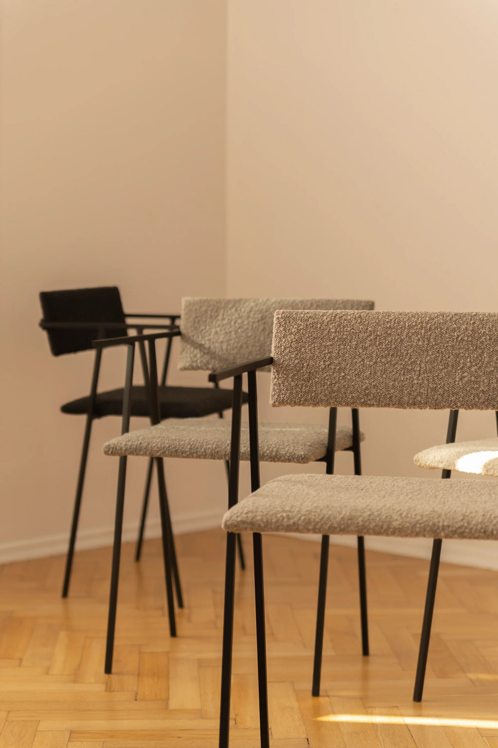 NG DESIGN Object 058 Chairs. Three modern chairs featuring subtly textured, light beige bouclé fabric upholstery on black metal frames, with one black chair in the background. Perfect for contemporary dining or office spaces.