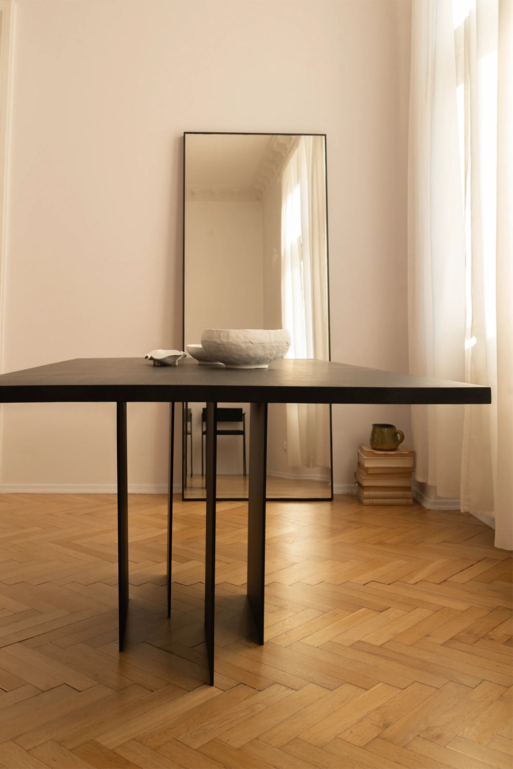 NG DESIGN Object 056 Dining Table, a luxurious, dark wood rectangular table with sleek black panel legs, displayed in a bright room with a mirror and white sheer curtains. Perfect for modern living spaces.