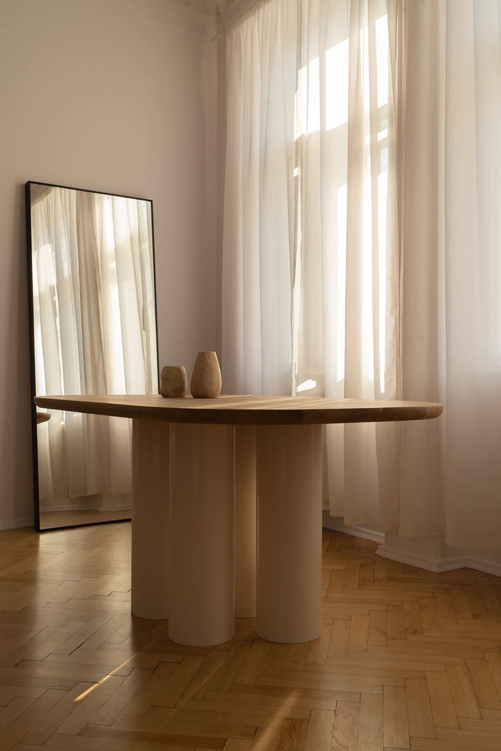 NG DESIGN Object 055 Dining Table, featuring a natural light-toned wooden top and three thick, matte cream cylindrical legs. Two textured beige decorative vases adorn the top in a bright, modern living room setting. A premium statement piece for contemporary interiors.