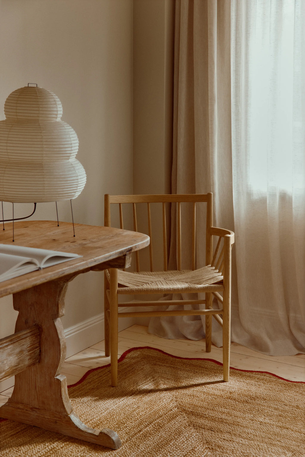 Wooden table with a chair in a room with curtains and a lamp.