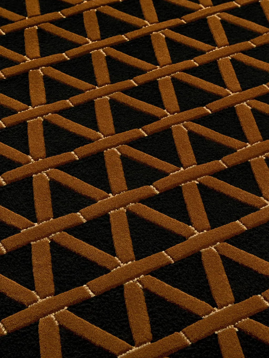 alp_ Secadero Rug, a striking black and brown geometric rug featuring a bold interlocking Art Deco-inspired pattern with textured tufted pile in rich cognac brown against a deep black background, accented by subtle cream-colored lines. This contemporary area rug is perfect for adding a sophisticated graphic statement to modern living rooms or elegant dining spaces.