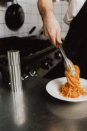 Person serving spaghetti onto a plate in a kitchen setting