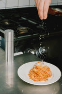 Person seasoning spaghetti on a plate with a salt grinder in a kitchen setting.